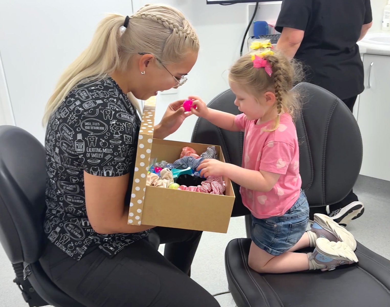 Young girl sitting up on dental chair to look in treasure chest.